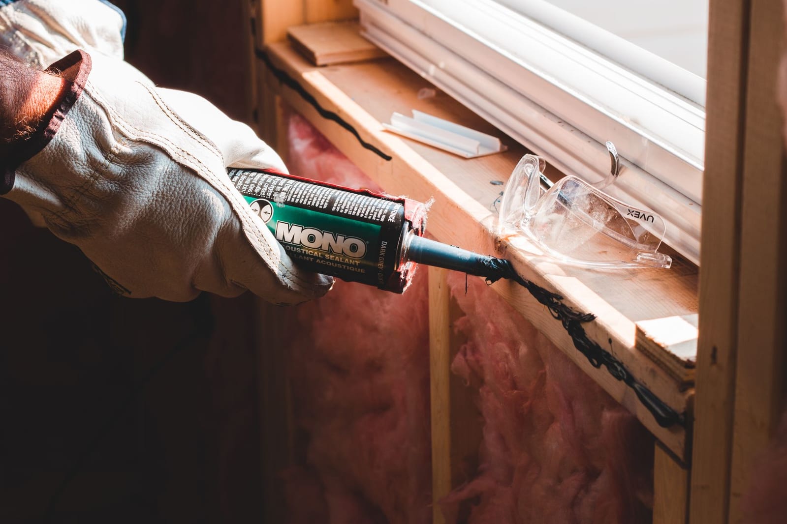A gloved technician caulking a gap around a window frame — sealing the entry points pests use to get inside